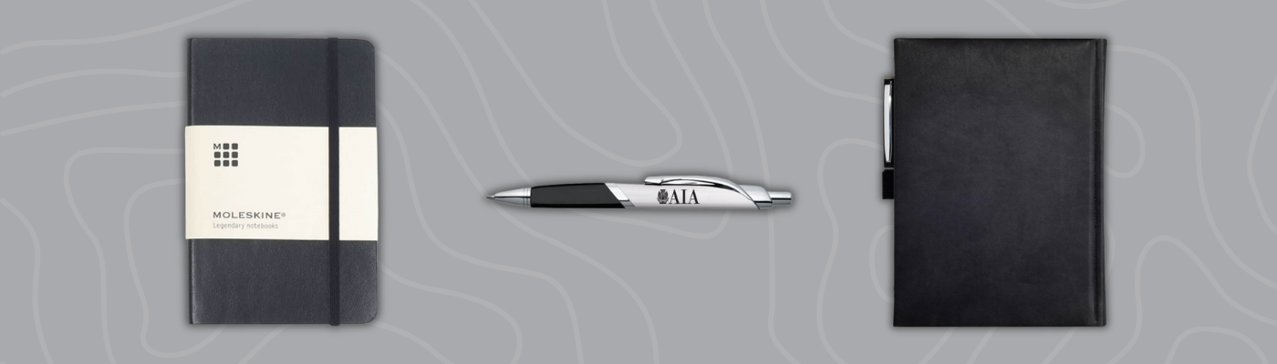 Black Moleskine notebook, branded pen, and leather journal displayed on gray background