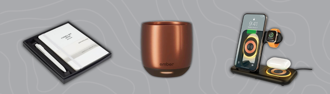 Custom corporate gifts including Ember smart mug, wireless charging stand, and Moleskine notebook set on gray background