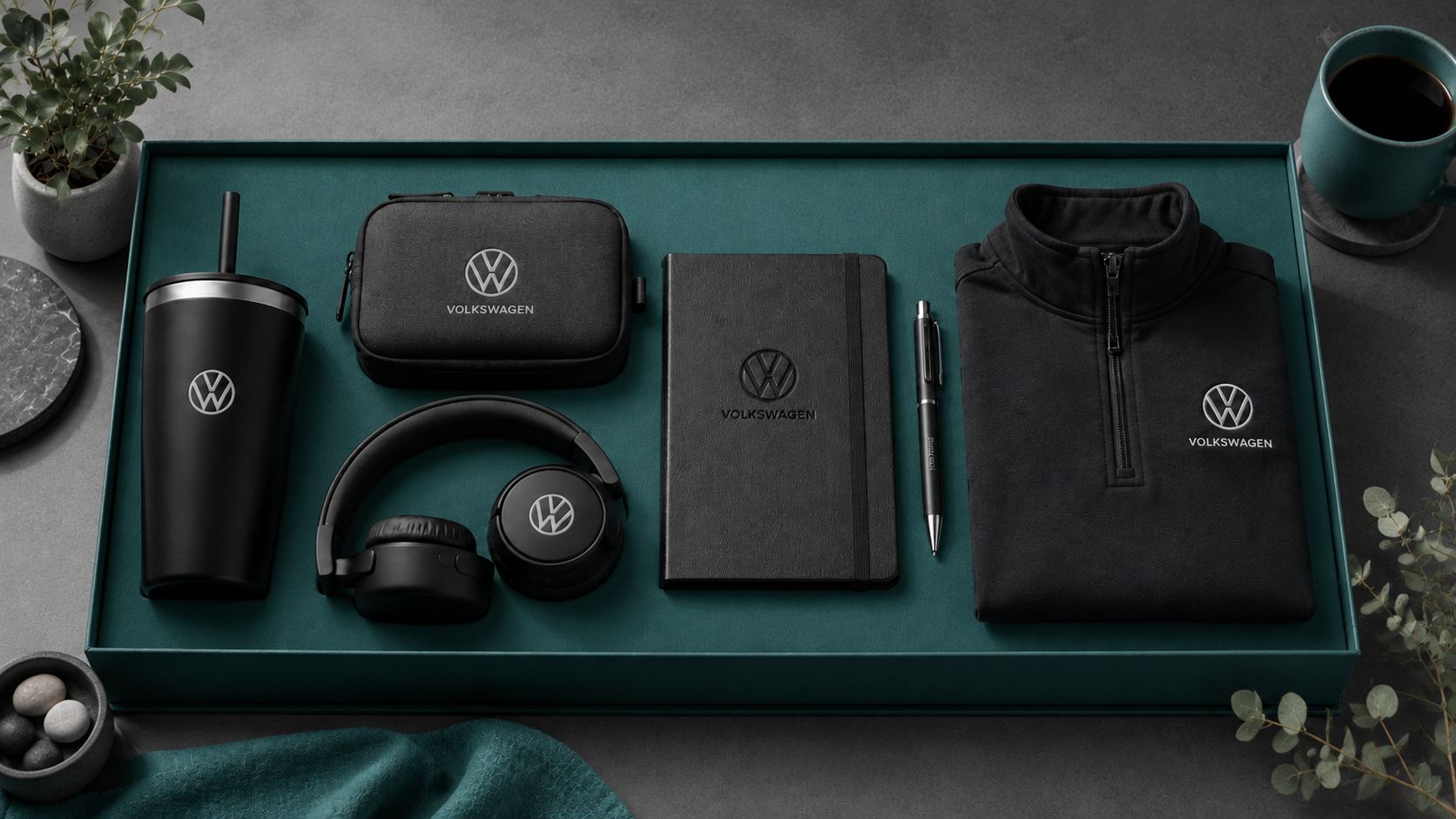 Volkswagen branded employee welcome kit with black tumbler, headphones, travel pouch, notebook, pen, and pullover arranged in a beige gift box.