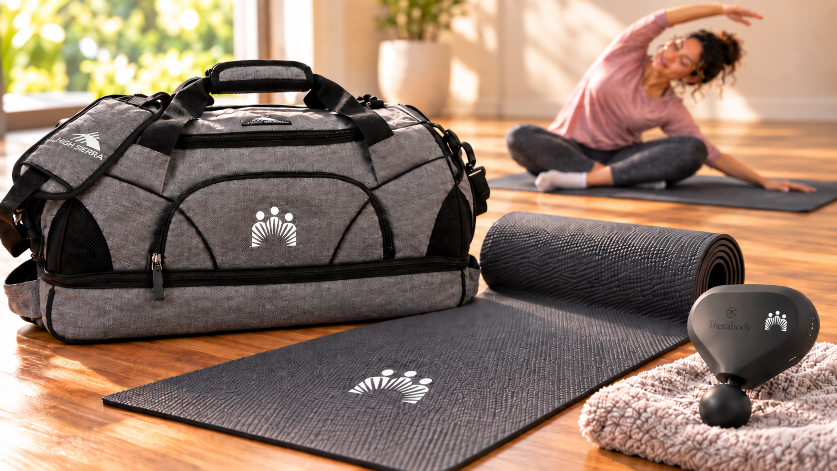 Best remote employee gifts featuring a gray High Sierra 24 inch Sport Duffel, a black USA Made Yoga Mat, and a black Theragun Mini 3rd Generation with company logos, while a remote employee stretches on a yoga mat in a bright home workout space.